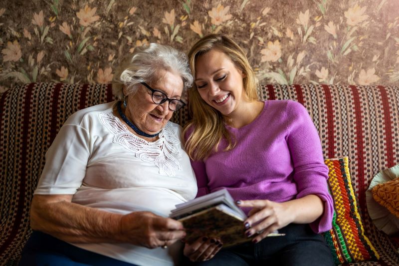 Senior and caregiver looking through photo albums on the couch